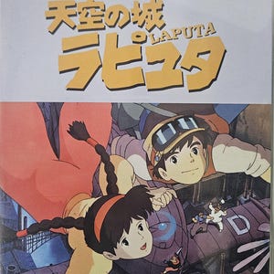 Op de afbeelding: DVD-hoesje met de animatiefilm "Castle in the Sky" (Laputa). De cover toont twee hoofdpersonages en de titel van de film in grote, gestileerde letters. De dvd-hoes zit in een doorzichtige plastic hoes.