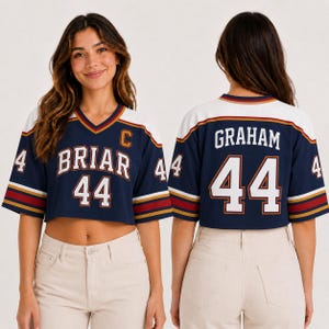 May include: Cropped navy blue jersey with white and gold accents. The jersey features the name "BRIAR" and the number "44" on the front, and "GRAHAM" and "44" on the back. The jersey has a V-neck and short sleeves.