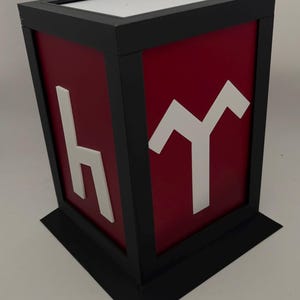 May include: A red and black decorative box with white lettering. The box has a black frame and base, with a white top. The red sides feature white letter shapes. The box is a unique decorative item.