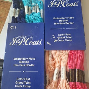May include: An assortment of J&P Coats embroidery floss in various colors. The image shows blue, teal, peach, and pink floss in their original packaging. The packaging includes the text "Embroidery Floss, Mouliné, Hilo Para Bordar, Color Fast, Grand Teint, Color Firme."
