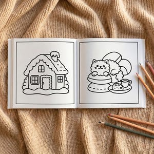 May include: A colouring book open at two pages with black and white illustrations. One shows a gingerbread house, the other a cat on a macaron with tea and biscuits. Coloured pencils are on the right.