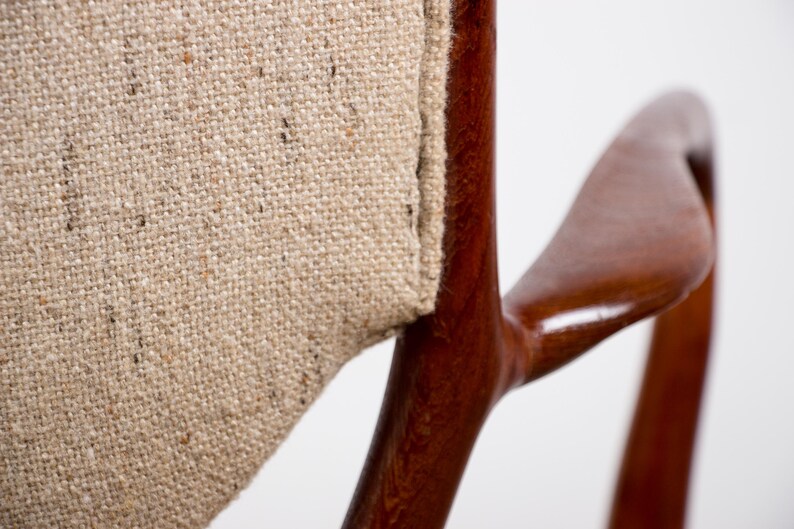 May include: Close-up of a wooden chair arm and backrest. The chair features a light brown, textured fabric and a dark, glossy wooden frame. The design is minimalist and the wood has a curved shape.