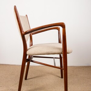 May include: A mid-century modern armchair with a wooden frame and armrests. The chair features a light-colored, textured seat and backrest. The wood has a rich, dark brown finish, and the chair is set against a neutral background.