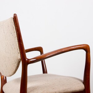 May include: A mid-century modern armchair with a curved wooden frame and a light-colored fabric seat and back. The chair has armrests and a minimalist design, showcasing the natural wood grain.