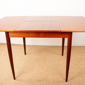 May include: A rectangular wooden dining table in a reddish-brown hue. The table features a central section and two side leaves. It rests on four tapered legs, showcasing a mid-century modern design. The table is approximately 122 cm wide and 76 cm tall.