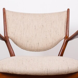 May include: A mid-century modern armchair with a curved back and armrests. The chair features a light beige fabric seat and backrest, and a dark wood frame. The design is minimalist and elegant, suitable for living room or office.