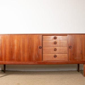 Könnte beinhalten: Ein Sideboard aus Holz im Mid-Century-Modern-Stil mit warmem, rötlich-braunem Finish. Der Schrank hat vier Schubladen mit runden Griffen und zwei Türen mit passenden Griffen. Er steht auf vier konischen Beinen.