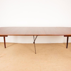 Op de afbeelding: Een eettafel in mid-century modern stijl met een rechthoekig, uitschuifbaar blad van hout. De tafel heeft vier taps toelopende poten en een centrale steun. De tafel is ongeveer 183 cm lang.