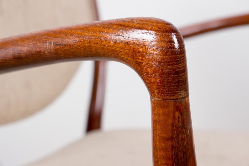 May include: Close-up of a wooden armchair armrest. The armrest is made of polished, reddish-brown wood with a curved design. The chair has a light-colored fabric seat and back.