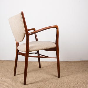 May include: A mid-century modern armchair with a curved back and armrests. The chair features a wooden frame with a warm, reddish-brown finish. The seat and back are upholstered in a light beige fabric.