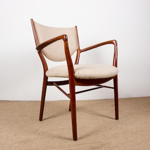 May include: Mid-century modern armchair with a curved wooden frame and light-colored fabric seat and back. The chair has armrests and a rounded seat, showcasing a minimalist design. The wood has a warm, reddish-brown tone.