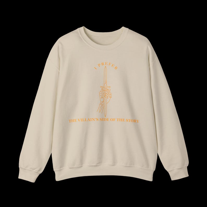 K&ouml;nnte beinhalten: Cremefarbenes Sweatshirt mit langen &Auml;rmeln. Auf der Vorderseite befindet sich eine orangefarbene Illustration einer Skeletthand, die ein Schwert h&auml;lt, mit dem Text "I PREFER THE VILLAIN'S SIDE OF THE STORY" in Orange.