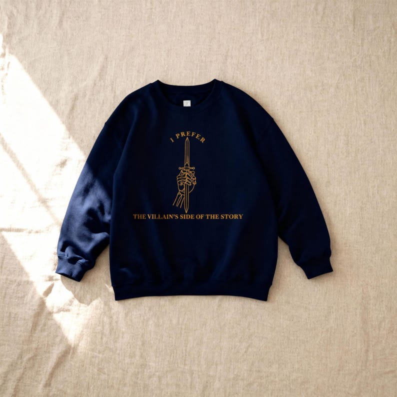 K&ouml;nnte beinhalten: Marineblaues Sweatshirt mit goldenem Text und Grafik. Der Text lautet "I PREFER THE VILLAIN'S SIDE OF THE STORY" &uuml;ber einer Grafik einer Skeletthand, die ein Schwert h&auml;lt. Das Sweatshirt ist ein Rundhals-Stil.