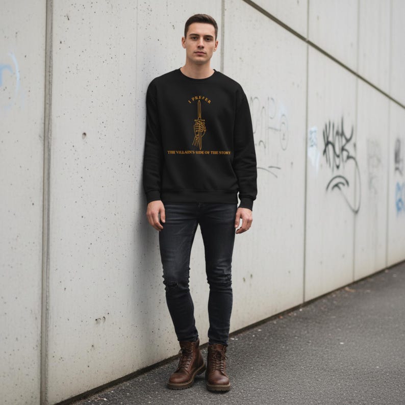 K&ouml;nnte beinhalten: Schwarzes Sweatshirt mit goldenem Text "I Prefer The Villain's Side of the Story" und einer Grafik einer Skeletthand, die ein Schwert h&auml;lt. Das Design befindet sich mittig auf der Brust.