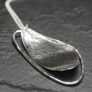 May include: A silver necklace with a hammered, oval-shaped pendant. The pendant is suspended from a thin silver chain and has a smooth, polished finish.
