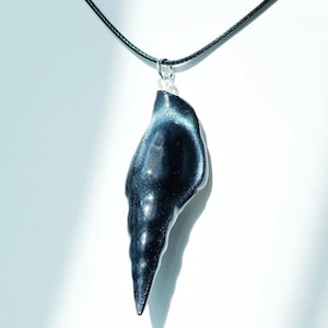 May include: A dark, iridescent pendant necklace. The pendant is a teardrop shape with a textured surface and a silver-coloured bail. The necklace cord is black.
