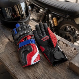 Może przedstawiać: Para rękawic motocyklowych w kolorach czarnym, czerwonym, białym i niebieskim. Rękawice posiadają ochraniacze kostek w stylu włókna węglowego, regulowane paski na nadgarstki oraz wzmocnioną wyściółkę dłoni z przeszyciami na palcach.