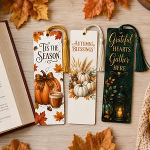 May include: Three rectangular bookmarks with tassels. The first is white with orange leaves, a pumpkin, and the text 'Tis the Season'. The second is white with wheat, pumpkins, and 'Autumn Blessings'. The third is dark green with a lantern and 'Grateful Hearts Gather Here'.