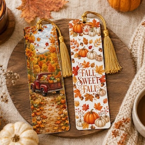 May include: Two rectangular bookmarks with gold tassels. One features a red truck carrying pumpkins through an autumn forest. The other displays orange and red maple leaves, pumpkins, acorns, and the text FALL SWEET FALL in brown script lettering.