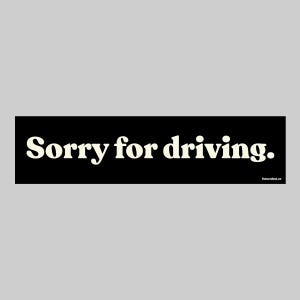 May include: A black rectangular bumper sticker with the text "Sorry for driving." in a bold, off-white font. The sticker has rounded corners and a website address in the bottom right corner.