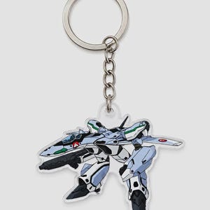 以下が含まれることがあります： 透明なアクリル製のキーホルダー。緑のアクセント、黒いコックピット、ダークグレーの武器を備えた、水色と白のロボット戦闘機のイラストがプリントされており、銀色の金属製リングと短いチェーンで連結されています。