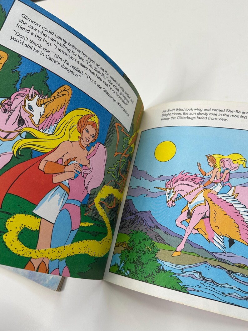 May include: A vintage comic book illustration featuring She-Ra and a pink unicorn with wings. The artwork is colorful, with text bubbles and a vibrant landscape. The text reads, "Thank the Glitterbugs. Without them you'd still be in Catra's dungeon."