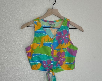 May include: A sleeveless crop top with a tie front. The top is made of a light fabric and has a colorful floral print with yellow, green, blue, pink, and purple hues.