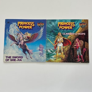 May include: Two vintage "Princess Power" comic books. The first cover features a character riding a winged horse, with the text "The Sword of She-Ra." The second cover shows a woman with a sword, with the text "Glimmer of Hope."