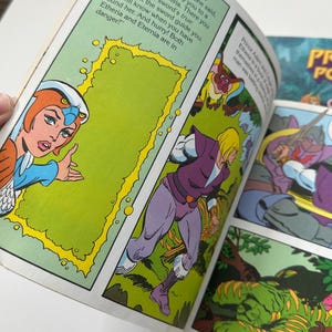 May include: Comic book page featuring colorful illustrations. The Sorceress points to a magical door, with text that reads "This portal will carry you to a planet called Etheria." Other panels show a running figure and a sword-wielding character.
