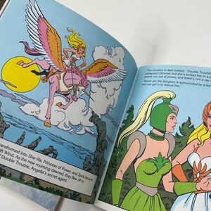 May include: Open book illustration featuring a blonde woman riding a pink unicorn with large pink and white wings. The background is blue with a yellow sun and white clouds. Text on the page reads "transformed into She-Ra, Princess of Power..."