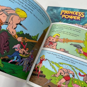 May include: Open comic book pages featuring illustrations of He-Man and other characters in action. The text includes phrases like "Princess Power" and "Sword of Protection". The artwork is colorful and in a classic comic book style.