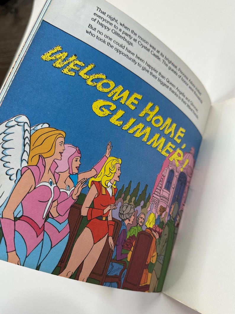 May include: An illustration from a children's book features the text "WELCOME HOME, GLIMMER!" in yellow letters against a blue sky. Several cartoon characters are depicted, including women in pink and red outfits, and a castle is visible in the background.