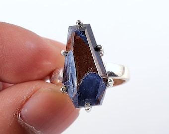 Op de afbeelding: Een zilveren ring met een grote, facetgeslepen edelsteen in diepblauwe en bruine tinten. De edelsteen heeft een ongewone, langwerpige vorm en is versierd met kleine zilveren studs. De ring heeft een eenvoudige, gepolijste zilveren band.
