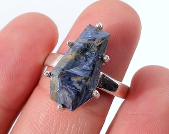 Op de afbeelding: Een zilveren ring met een rechthoekige, blauwe en gele edelsteen. De edelsteen heeft een unieke, getextureerde uitstraling en is gezet met kleine, zilveren accenten. De ring wordt gepresenteerd tegen een witte achtergrond.
