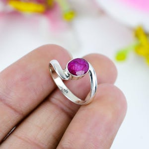 May include: A sterling silver ring featuring a vibrant, oval-cut ruby gemstone. The ring has a modern, flowing design with a polished finish. The ruby is a deep, rich pink color, set in a simple bezel setting.