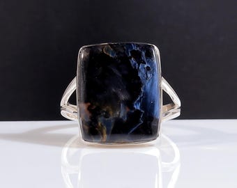 May include: A rectangular gemstone ring with a silver band. The gemstone is a deep blue with streaks of gold and brown. The ring's band has a split design on each side of the gemstone.