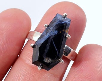 Op de afbeelding: Zilveren ring met een donkerblauwe en zwarte edelsteen in een geometrische, kistachtige vorm. De edelsteen heeft een gemarmerd uiterlijk met gouden vlekken. Kleine zilveren accenten rond de steen.