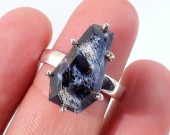 May include: A silver ring featuring a dark blue gemstone with white and gold veining. The gemstone is cut into a unique, elongated hexagonal shape and is accented with small silver studs.