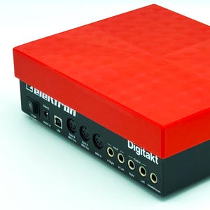 May include: An Elektron Digitakt drum machine and sampler with a bright red top cover and a black base. The rear panel features a power switch, 12V DC input, USB port, MIDI Thru, Out, and In ports, plus audio inputs and outputs labelled in white text.