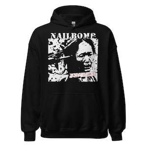 May include: Black hooded sweatshirt featuring a graphic design. The design includes the word "NAILBOMB" in white, above a black and white image of a person. The text "POINT BLANK" is in a red rectangle below the image.