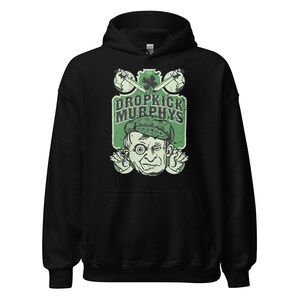 May include: Black hooded sweatshirt featuring a green and white graphic. The graphic includes the text "DROPKICK MURPHYS" above a cartoon illustration of a man wearing a green hat. Two crossed instruments are above the text.