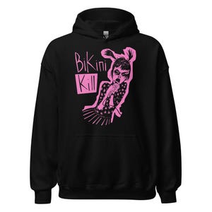 May include: Black hooded sweatshirt featuring a pink graphic of a person singing into a microphone, with the words "Bikini Kill" in pink. The graphic is a stylized illustration. The sweatshirt has a drawstring hood and a kangaroo pocket.