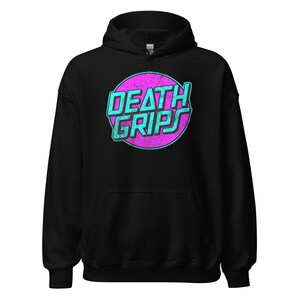 May include: Black hooded sweatshirt with the text "DEATH GRIPS" in a teal and pink retro design. The graphic is inside a pink circle. The sweatshirt has a drawstring hood and a front pocket.