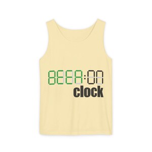 May include: A pale yellow tank top featuring a digital clock graphic on the front. The display shows the text BEER:00 in a mix of green and black segmented digital font, with the word clock printed in black sans-serif letters underneath.