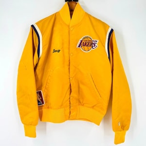 Puede incluir: Una chaqueta amarilla vintage de Los Angeles Lakers con cierre de botones, con el logo de los Lakers y el nombre "Doug" bordado en el pecho. La chaqueta tiene rayas azul marino y blancas en las mangas y un pequeño parche de la NBA.