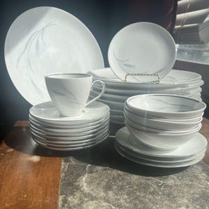 May include: A set of three ceramic mugs with a speckled, matte finish. The mugs are in shades of cream, light gray, and dark gray. Each mug has a simple, minimalist design, perfect for coffee or tea.