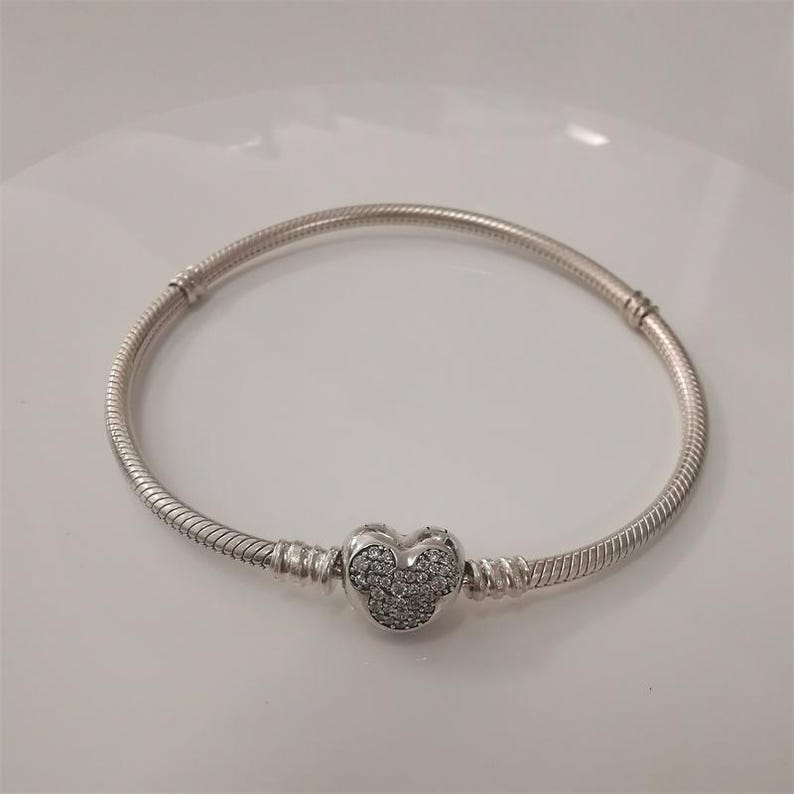 Puede incluir: Una pulsera plateada con un dije en forma de coraz&oacute;n. El dije est&aacute; incrustado con peque&ntilde;as piedras transparentes. La pulsera tiene un dise&ntilde;o de cadena de serpiente y un cierre. Una joya.