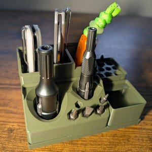 May include: An olive green organizer with compartments holding tools and accessories. The organizer has slots for screwdrivers, bits, and other small items. A green and yellow lanyard is attached to one of the tools.