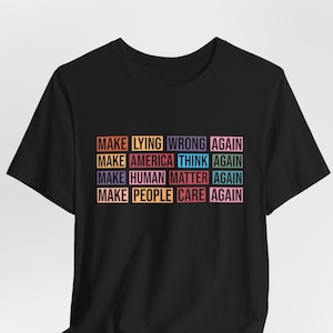 Może przedstawiać: Czarny t-shirt z krótkim rękawem z nadrukiem siatki kolorowych prostokątów z tekstem: MAKE LYING WRONG AGAIN, MAKE AMERICA THINK AGAIN, MAKE HUMAN MATTER AGAIN oraz MAKE PEOPLE CARE AGAIN, wydrukowanym w różnych wyrazistych kolorach.
