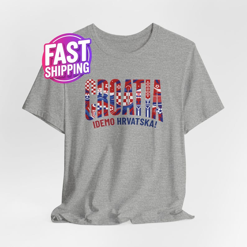 Peut inclure: Un t-shirt gris avec le mot "CROATIA" en rouge, blanc et bleu, avec divers motifs et dessins. En dessous, la phrase "IDEMO HRVATSKA!" en blanc. Un autocollant "FAST SHIPPING" est dans le coin sup&eacute;rieur gauche.